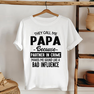 A white t-shirt with a humorous text printed on it, hanging on a wooden hanger.