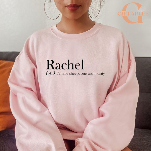 A woman wearing a pink sweatshirt with the word "Rachel" printed on it.