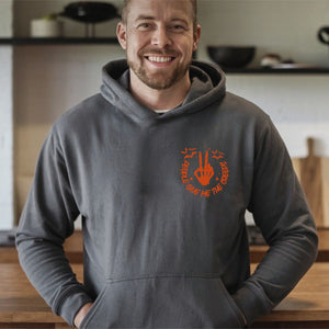 A man wearing a gray hoodie with an orange graphic and text on it, smiling at the camera.