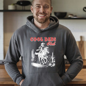A man wearing a grey hoodie with a graphic design of a cowboy on a horse and the text "Cool Dads Club" printed on it.