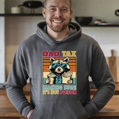 A man wearing a gray hoodie with a graphic design of a raccoon wearing sunglasses and holding a drink, along with the text "DAD TAX MAKING SURE IT'S NOT POISON".
