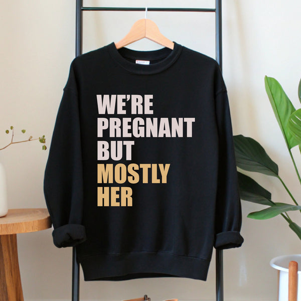 A black sweatshirt with white text printed on it, hanging on a wooden hanger.