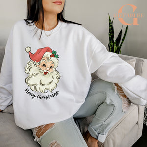 A woman wearing a white sweatshirt with a Santa Claus graphic and the text "Merry Christmas" printed on it, sitting on a couch.