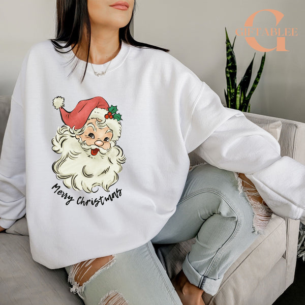A woman wearing a white sweatshirt with a Santa Claus graphic and the text "Merry Christmas" printed on it, sitting on a couch.