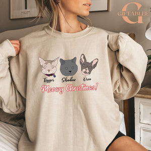 A woman wearing a beige sweater with a graphic design featuring three cat faces and the text "Meowy Christmas!"