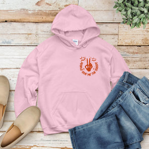 A pink hoodie with an orange graphic and text, a pair of blue jeans, and a pair of beige shoes are arranged on a wooden surface.
