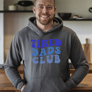 A man wearing a gray hoodie with the text "TIRED DADS CLUB" printed on it, smiling at the camera.