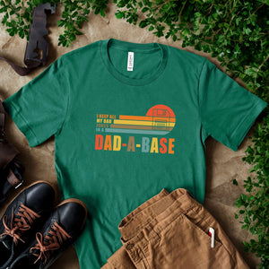 A green t-shirt with a graphic design, a pair of brown pants, and a pair of black shoes are arranged on a surface with some greenery.