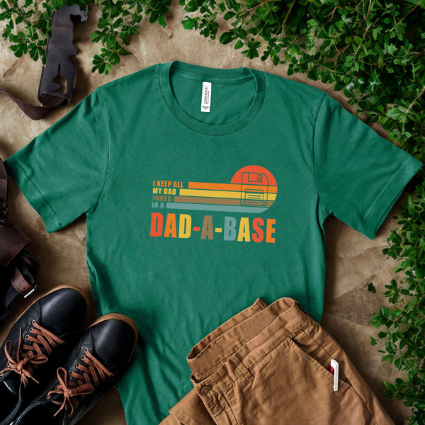 A green t-shirt with a graphic design, a pair of brown pants, and a pair of black shoes are arranged on a surface with some greenery.