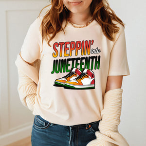 A woman wearing a white t-shirt with a graphic design featuring a pair of colorful sneakers and the text "StepPIN' into JUNETFEST".