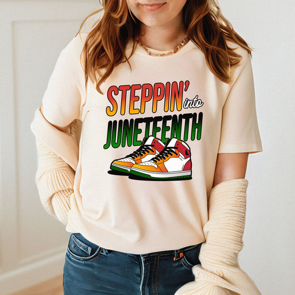 A woman wearing a white t-shirt with a graphic design featuring a pair of colorful sneakers and the text "StepPIN' into JUNETFEST".