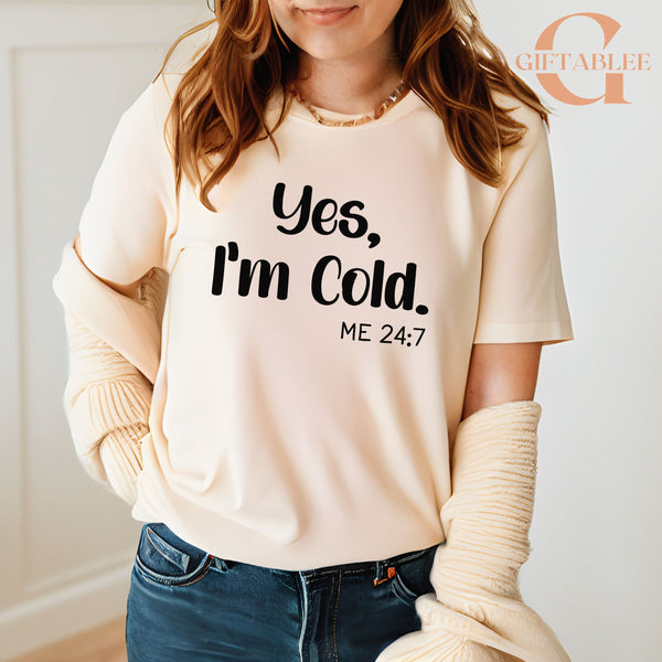 A woman wearing a white t-shirt with the text "Yes, I'm Cold. ME 24:7" printed on it.
