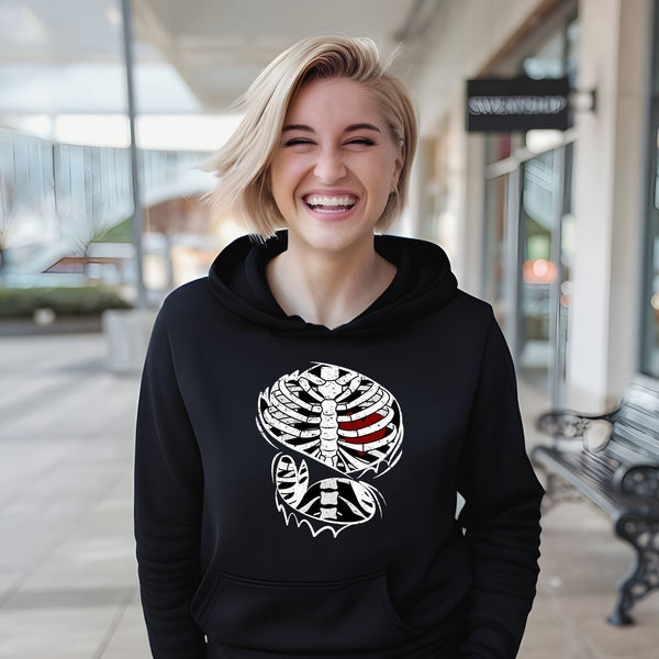 A smiling woman wearing a black hoodie with a graphic design on it, standing in front of a building.