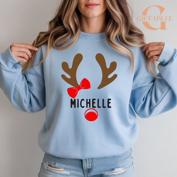 A woman wearing a light blue sweatshirt with a graphic design of a reindeer and the name "Michele" printed on it.