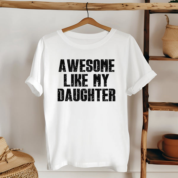 A white t-shirt with the text "AWESOME LIKE MY DAUGHTER" printed on it, hanging on a wooden hanger.