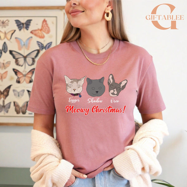 A woman wearing a pink t-shirt with a graphic design of three cat faces and the text "Meowy Christmas!" printed on it.