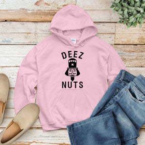 A pink hoodie with the text "DEEZ NUTS" printed on it, along with a nutcracker graphic, is displayed on a wooden surface.