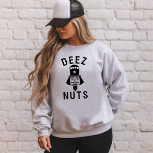 A woman wearing a sport gray sweatshirt with the text "DEEZ NUTS" printed on it, standing in front of a white brick wall.