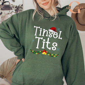 A woman wearing a green hoodie with the text "Tinsel Tits" printed on it.