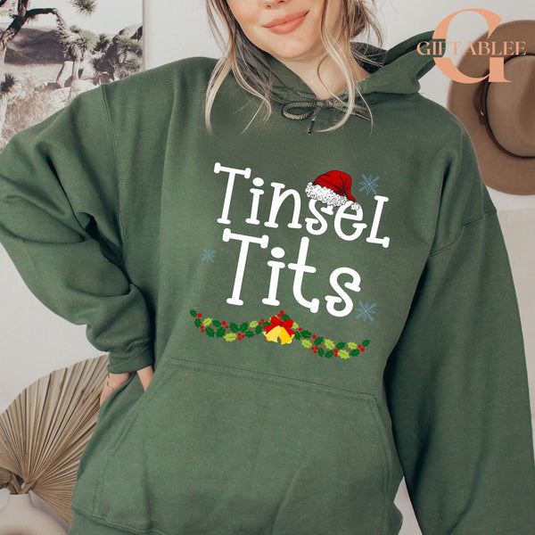 A woman wearing a green hoodie with the text "Tinsel Tits" printed on it.