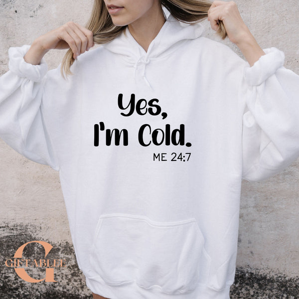 A person wearing a white hoodie with the text "Yes, I'm Cold. ME 24:7" printed on it.
