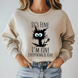 A woman wearing a beige sweater with a graphic design featuring a cat and the text "It's fine I'm fine everything is fine".