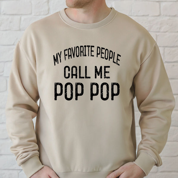 A man wearing a beige sweater with the text "MY FAVORITE PEOPLE CALL ME POP POP" printed on it.