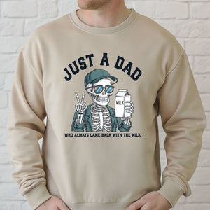 A man wearing a beige sweater with a graphic design depicting a skeleton wearing sunglasses and holding a carton of milk, along with the text "Just a Dad" and "Who always came back with the milk".