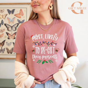 A woman wearing a pink t-shirt with a humorous Christmas-themed text printed on it, standing in front of a butterfly-themed wall art.