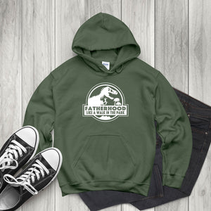 A green hoodie with a graphic and text printed on it, along with a pair of black and white sneakers and a pair of dark jeans, all laid out on a wooden surface.