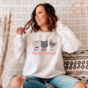 A woman wearing a white sweatshirt with a graphic design of three cat faces and the text "Meowy Christmas!"