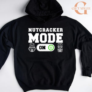 A black hoodie with a white text design that says "NUTCRACKER MODE ON" and two icons representing a robot and a power button.