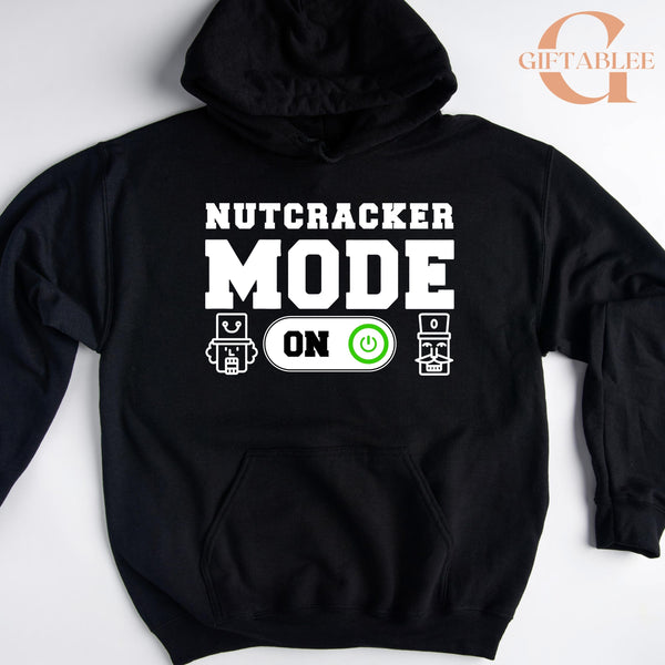 A black hoodie with a white text design that says "NUTCRACKER MODE ON" and two icons representing a robot and a power button.