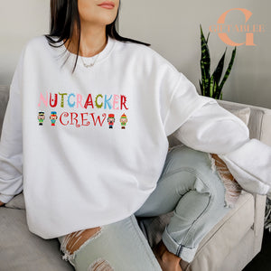 A woman wearing a white sweatshirt with the text "NUTCRACKER CREW" printed on it, sitting on a couch.