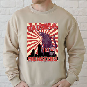 A man wearing a beige sweater with a graphic design featuring a large, menacing-looking creature resembling a Godzilla-like monster, along with the text "DADZILLA" and "FATHER OF MONSTERS".
