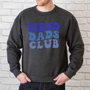 A man wearing a gray sweatshirt with the text "TIRED DAD'S CLUB" printed on it.