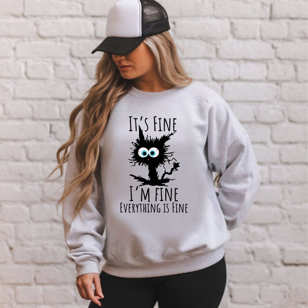 A woman wearing a gray sweatshirt with a black and white cat graphic and text that says "It's fine I'm fine everything is fine".