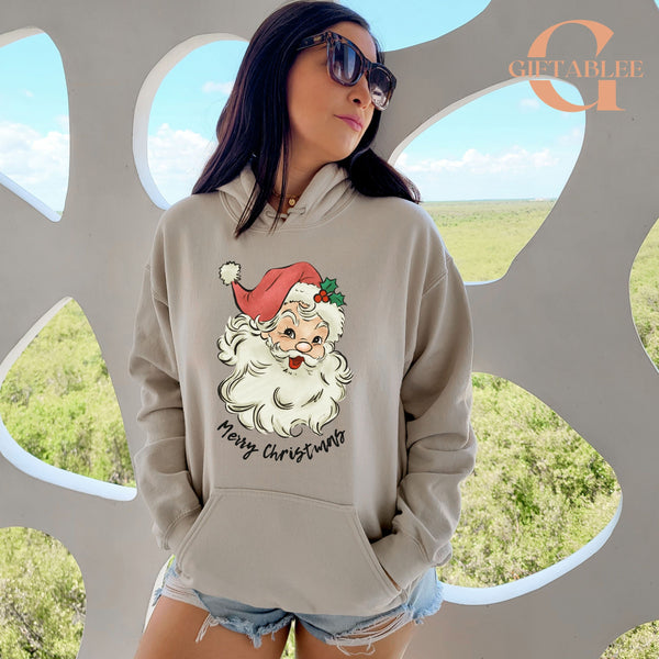 A woman wearing a grey hoodie with a Santa Claus graphic and the text "Merry Christmas" is standing in front of a window with a view of a field.