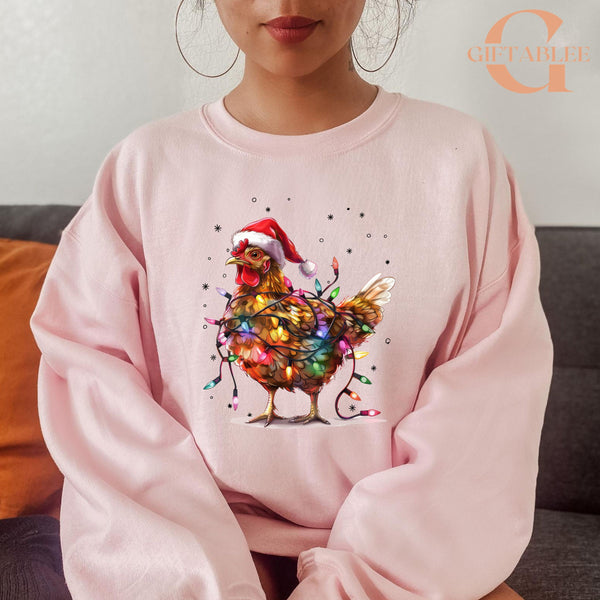 A woman wearing a pink sweatshirt with a colorful, festive image of a chicken wearing a Santa hat and surrounded by Christmas lights.