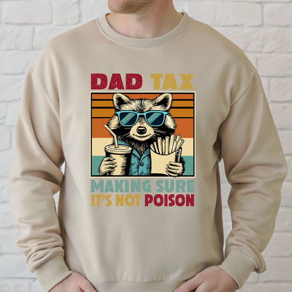 A man wearing a beige sweater with a graphic design featuring a raccoon wearing sunglasses and holding a drink, along with the text "DAD TAX MAKING SURE IT'S NOT POISON".