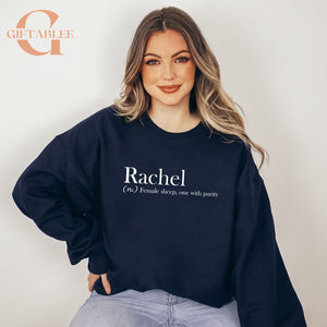 A woman wearing a navy blue sweatshirt with the word "Rachael" printed on it, posing for a portrait against a white background.