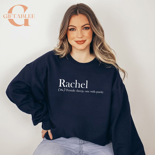 A woman wearing a navy blue sweatshirt with the word "Rachael" printed on it, posing for a portrait against a white background.