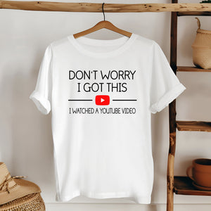 A white t-shirt with a humorous text printed on it, hanging on a wooden hanger.