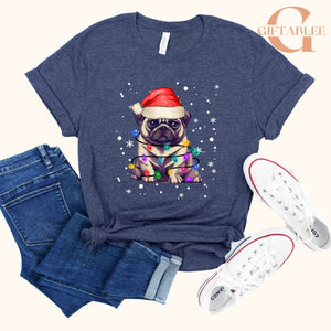 A gray t-shirt with a graphic of a pug wearing a Santa hat and surrounded by Christmas lights, along with a pair of jeans and white sneakers.