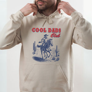 A man wearing a beige hoodie with a graphic design of a cowboy riding a horse in a desert landscape.