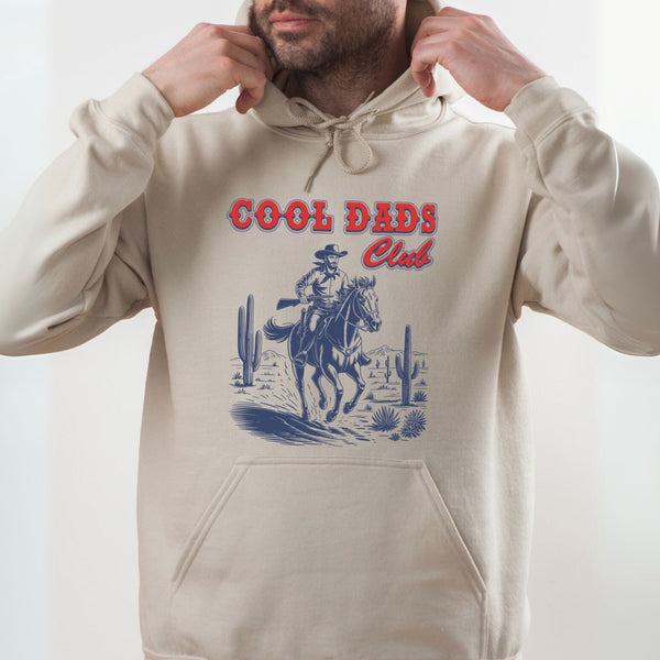 A man wearing a beige hoodie with a graphic design of a cowboy riding a horse in a desert landscape.