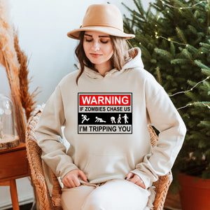 A woman wearing a beige hat and a white hoodie with a warning graphic on it, sitting in a chair in front of a Christmas tree.