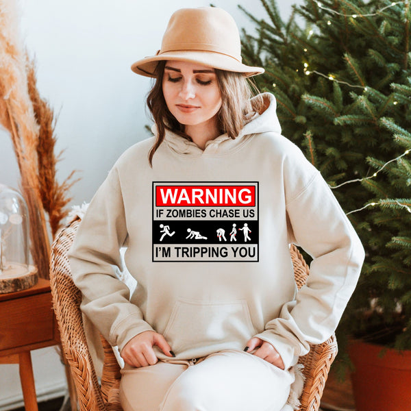 A woman wearing a beige hat and a white hoodie with a warning graphic on it, sitting in a chair in front of a Christmas tree.