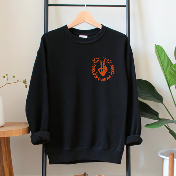 A black sweatshirt with an orange graphic and text printed on it, hanging on a wooden hanger.