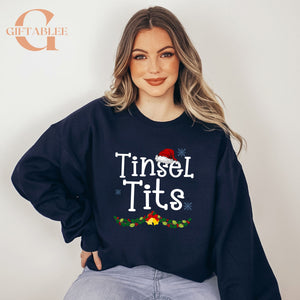 A woman wearing a navy blue sweatshirt with the text "Tinsel Tits" printed on it, smiling at the camera.